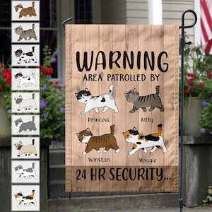 May include: A wooden-look garden flag with the words "WARNING AREA PATROLLED BY" and the names Princess, Kitty, Winston, and Maggie. The flag features cartoon cat illustrations and the text "24 HR SECURITY..."