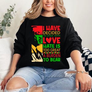 May include: Black sweatshirt with a red, yellow, green and black graphic print. The graphic features a portrait of a person with the text "I have decided to stick with love. Hate is too great a burden to bear."