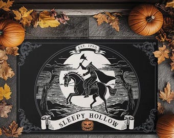 May include: Black doormat featuring a headless horseman riding a horse, with the text "Sleepy Hollow" and "Est. 1790". The design is surrounded by a decorative border and pumpkins. Autumn leaves and pumpkins frame the mat.