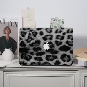 May include: A laptop case with a black and white leopard print pattern. The case has the Apple logo in white. The case is on a white surface.