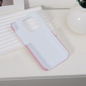 K&ouml;nnte beinhalten: Eine wei&szlig;e Handyh&uuml;lle mit rosa Rand. Die H&uuml;lle hat ein schlichtes, sauberes Design und besteht aus einem strapazierf&auml;higen Material. Die H&uuml;lle sch&uuml;tzt das Telefon vor Kratzern und anderen Besch&auml;digungen.