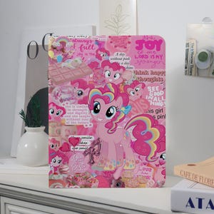 May include: Pink notebook featuring a cartoon pony with a rainbow mane and tail. The cover is a collage of pink elements, including hearts, cupcakes, and text. The text includes phrases like "The Joy of the Lord is My Strength" and "See Good in All Things."
