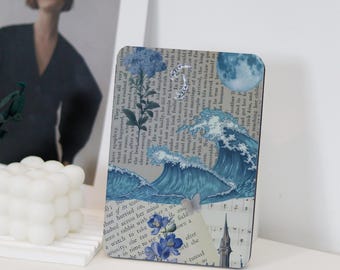 May include: A blue and white collage art print featuring a full moon, waves, and flowers. The print is on a textured paper background with a vintage aesthetic.