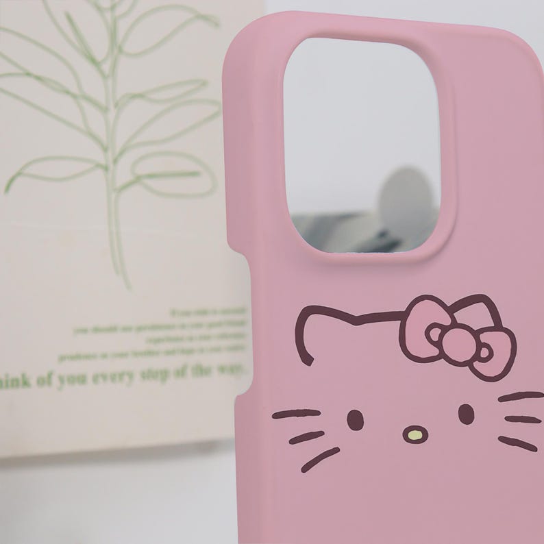 K&ouml;nnte beinhalten: Eine rosa Handyh&uuml;lle mit einem Cartoon-Katzen-Gesicht-Design. Die H&uuml;lle hat einen Kameraausschnitt und eine glatte Oberfl&auml;che. Das Katzengesicht hat Schnurrhaare, eine Nase und eine Schleife.