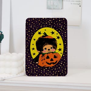 May include: A rectangular tablet case featuring a dark purple background covered in small gold stars. A central yellow oval contains a graphic of a brown-haired character with a small tuft of hair holding a large orange jack-o'-lantern pumpkin.