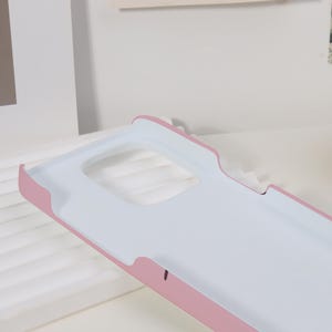 K&ouml;nnte beinhalten: Hellrosa und wei&szlig;e Handyh&uuml;lle mit rechteckigem Kameraausschnitt. Die H&uuml;lle hat eine glatte, matte Oberfl&auml;che und ein geschwungenes Design. Die Innenseite ist wei&szlig; und die Au&szlig;enkanten sind hellrosa.