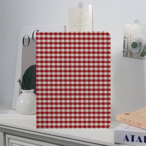 May include: A rectangular notebook with a red and white checkered pattern. The notebook is standing upright on a white surface. The notebook is the focal point of the image.