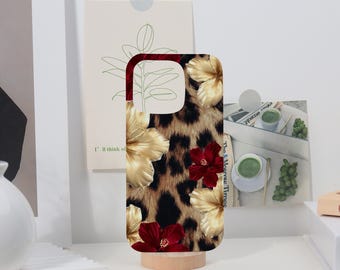 May include: A phone case featuring a leopard print design with gold and red hibiscus flowers. The case is displayed on a wooden stand, showcasing its vibrant colors and floral pattern. The case is designed to fit a smartphone.