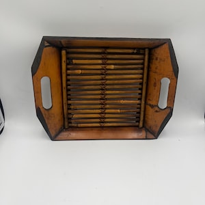 May include: A rectangular bamboo tray with a dark brown border and cut-out handles. The tray's interior features parallel bamboo slats, creating a textured surface. The tray is a warm, natural brown color.