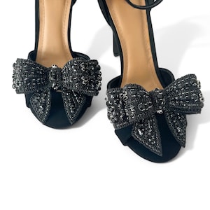 May include: A pair of black heeled sandals with a large black jeweled bow on the toe of each shoe.