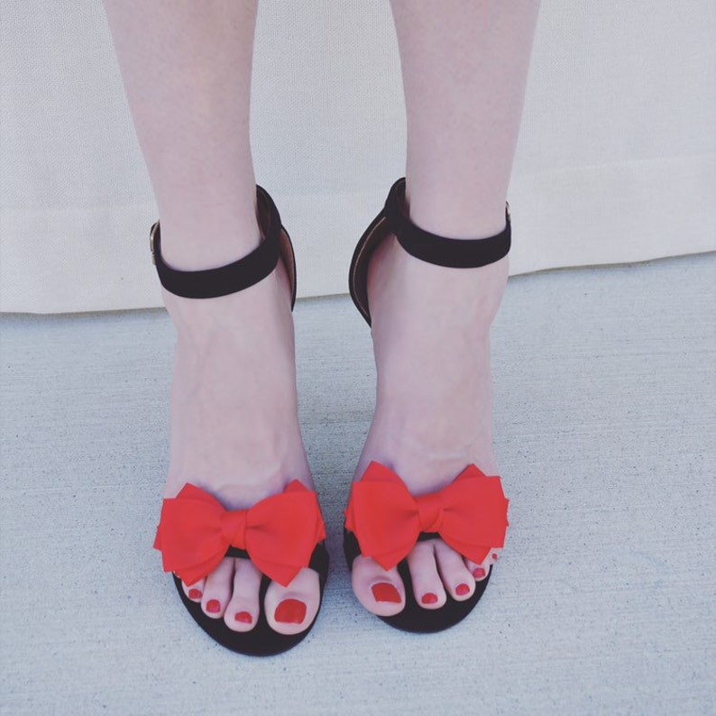 May include: Black heeled sandals with red bows on the toes. The sandals have a thin ankle strap.