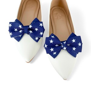 May include: A pair of white ballet flats with navy blue bows. The bows are made of fabric with white stars printed on them.