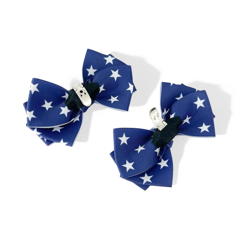 May include: Two blue hair clips with white stars. The clips are made of ribbon and have a metal clip on the back.