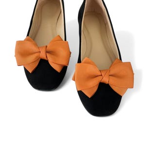 May include: A pair of black suede ballet flats with orange satin bows on the toes.