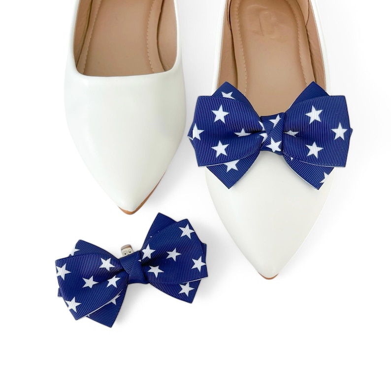 May include: A pair of white ballet flats with navy blue and white star patterned bows. The bows are attached to the shoes with a clip.