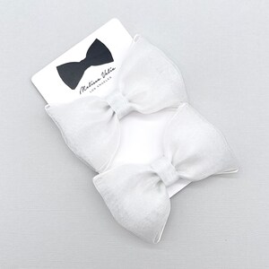 May include: Two white satin ribbon bows with a white card behind them. The card has the text "Melissa Vale, Los Angeles" printed on it.