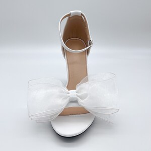 May include: White high-heeled sandals with a large white bow made of tulle.