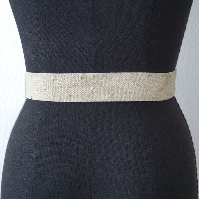 May include: A beige elastic belt with gold glitter woven into the fabric.