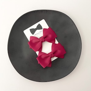 May include: Two burgundy grosgrain ribbon hair bows with a white card that says "Madeline Vedia Los Angeles" in black text.