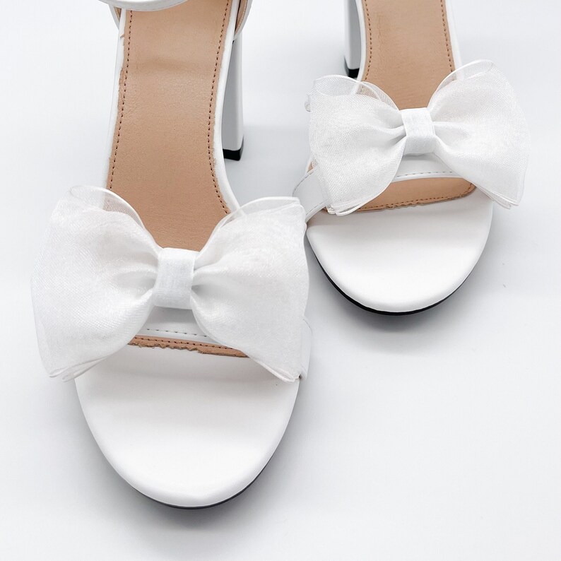 May include: White heeled sandals with a white bow on each strap.