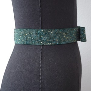 May include: A green and gold sparkly elastic belt with a bow on the side.