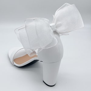 May include: White heeled sandals with a large white bow made of tulle.