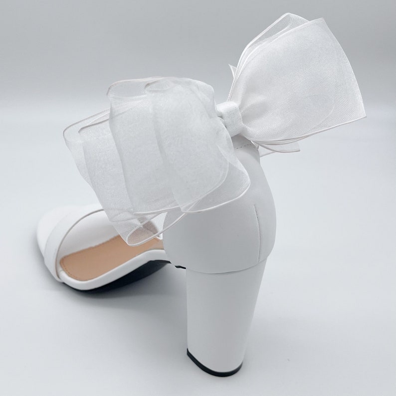 May include: White heeled sandals with a large white bow made of tulle.