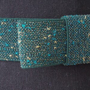May include: A close-up of a dark green elastic band with gold and teal glitter woven into the fabric.