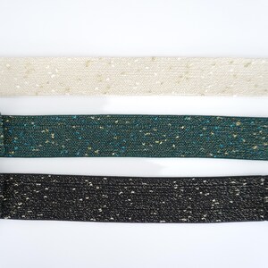 May include: Three different colours of elastic ribbon with gold glitter. The colours are beige, teal, and black.