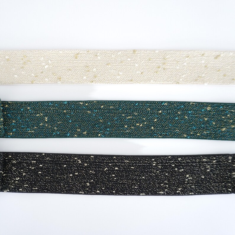 May include: Three different colours of elastic ribbon with gold glitter. The colours are beige, teal, and black.