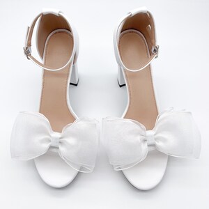 May include: White bridal heels with a large white bow on the front of each shoe.