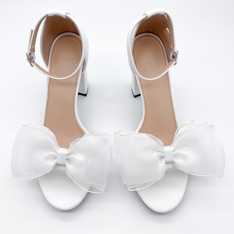 May include: White bridal heels with a large white bow on the front of each shoe.