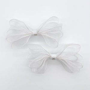 May include: Two white sheer ribbon bows with a small silver accent in the center of each bow.