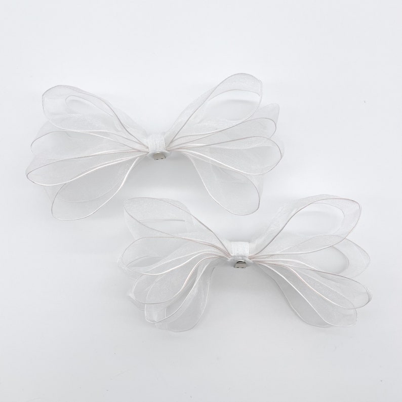 May include: Two white sheer ribbon bows with a small silver accent in the center of each bow.