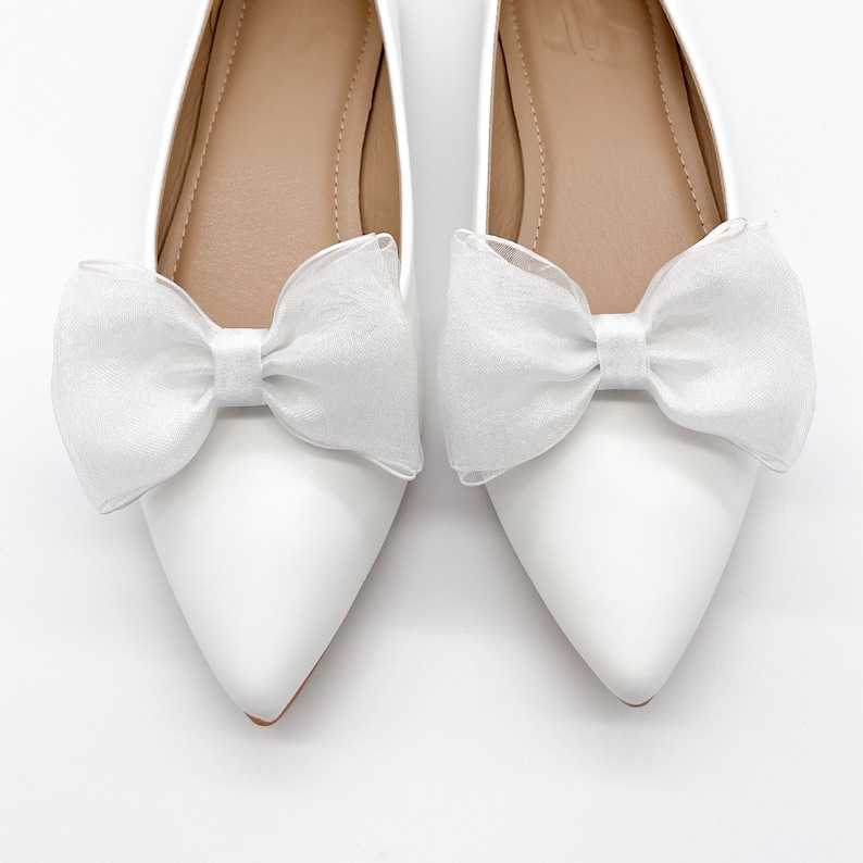 May include: A pair of white ballet flats with a white tulle bow on each shoe.
