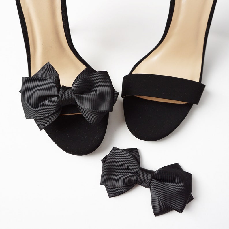 May include: A pair of black heeled sandals with a black satin bow on each strap. A separate black satin bow is also included.