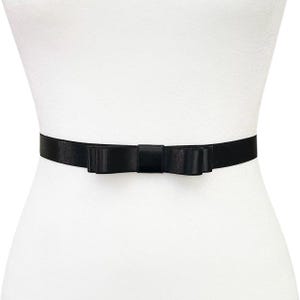May include: A black satin bow belt. The belt features a small bow in the center and a thin band. The belt is displayed on a white mannequin.