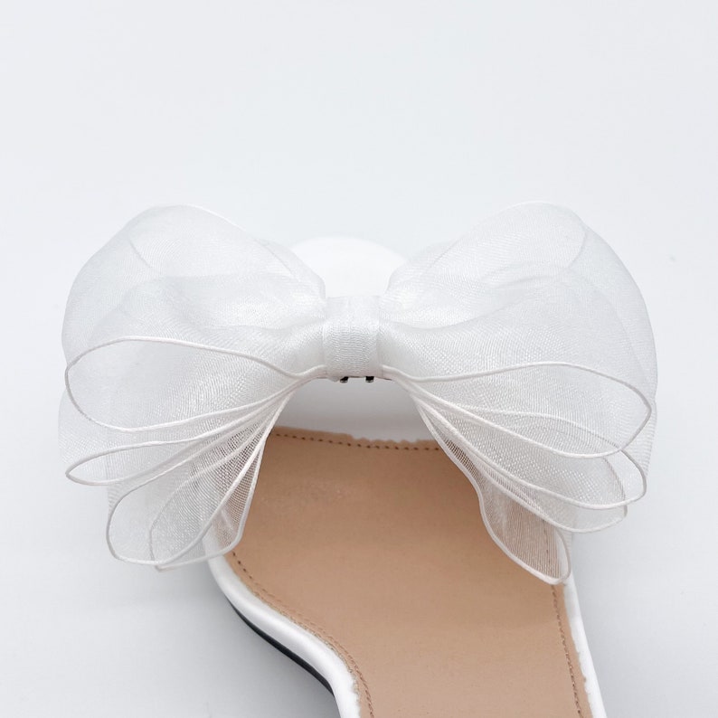 May include: White satin heeled sandals with a large white tulle bow on the top.