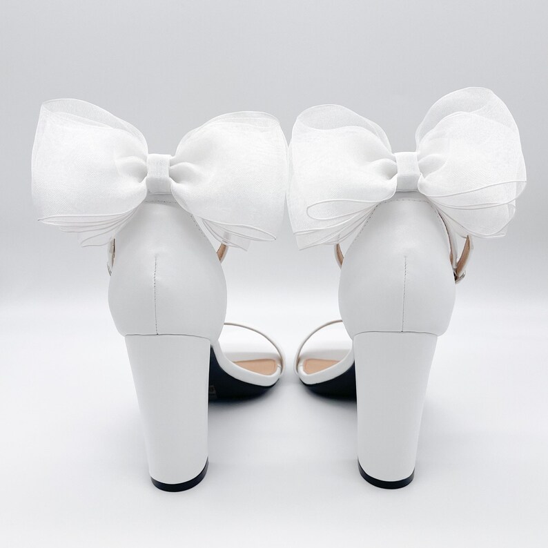 May include: White high-heeled sandals with a large white bow on each ankle strap.