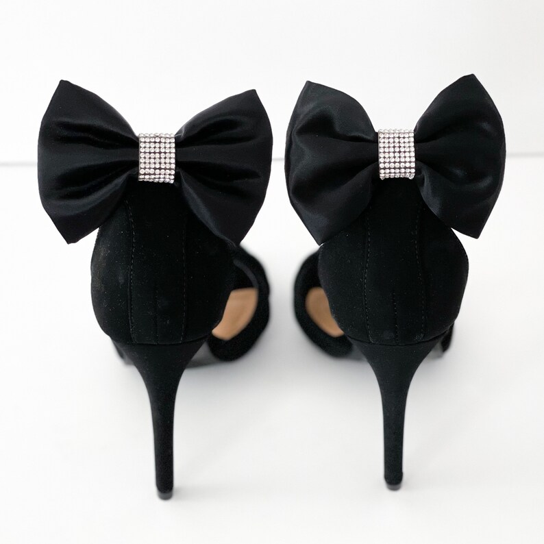 Puede incluir: Un par de zapatos negros de tac&oacute;n alto con lazos de sat&eacute;n negro y adornos de pedrer&iacute;a.