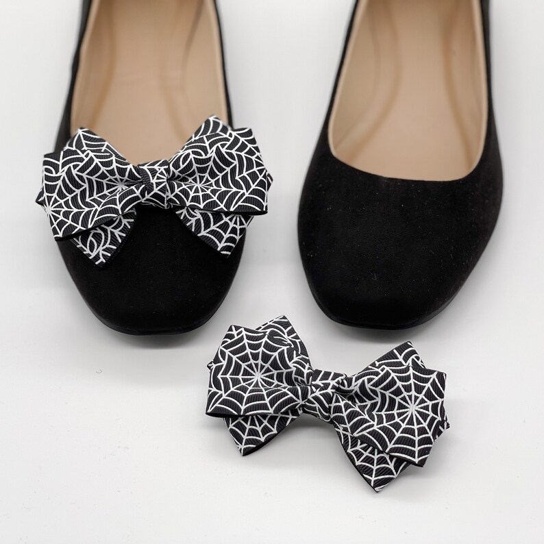 Pode incluir: Dois pares de sapatilhas de bal&eacute; pretas com um la&ccedil;o de teia de aranha branca em cada sapato. Um par de sapatos est&aacute; sobre uma superf&iacute;cie branca e o outro par est&aacute; sobre uma superf&iacute;cie branca.