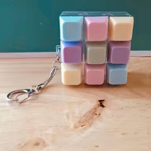 May include: A square keyring featuring a grid of nine pastel-coloured keycaps in shades of blue, pink, yellow, and purple. The keycaps are arranged in a three-by-three pattern within a clear frame, attached to a silver-toned metal split ring.