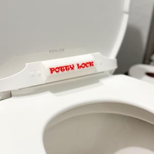 May include: White toilet seat with a white plastic child safety lock labelled "POTTY LOCK" in red letters.