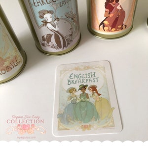 May include: A white card with a decorative border and the text "English Breakfast" in black lettering. Three women in vintage dresses are depicted drinking tea. The card is part of an "Elegant Tea Lady Collection".