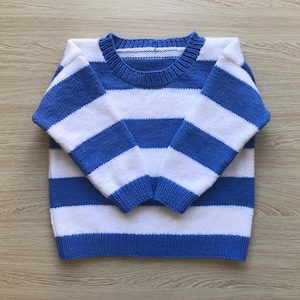May include: A blue and white striped sweater. The sweater has a crew neck and long sleeves. The stripes are horizontal and alternate between blue and white. The sweater is folded neatly on a wooden surface.