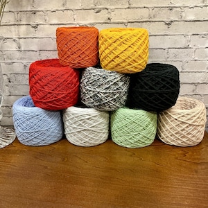 May include: A collection of colorful yarn skeins in various shades, including orange, yellow, red, gray, black, blue, white, and green. The yarn is neatly arranged, showcasing the texture and color variations. Ideal for knitting and crochet projects.