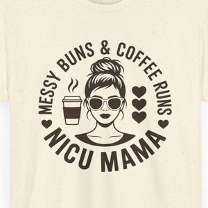 Puede incluir: Camiseta color crema con un diseño circular. El diseño presenta a una mujer con gafas de sol, una taza de café y el texto "Messy Buns & Coffee Runs NICU Mama" en un círculo con corazones.