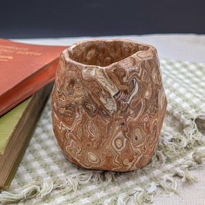 May include: A brown and white marbled ceramic planter with a rough, textured surface. The planter is shaped like a rounded cup.