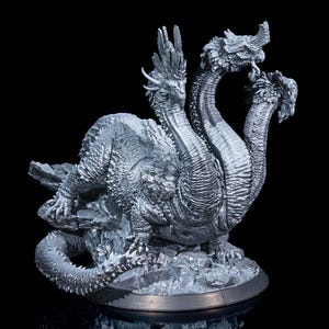 Puede incluir: Una detallada escultura plateada de un dragón de tres cabezas. El dragón está posicionado sobre una base rocosa, con escamas intrincadas y detalles texturizados. La escultura se encuentra sobre un fondo negro.