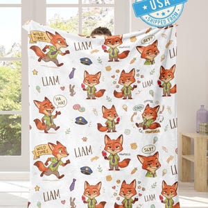 K&ouml;nnte beinhalten: Wei&szlig;e Decke mit einem sich wiederholenden Muster eines Cartoon-Fuchs-Charakters in verschiedenen Posen. Der Fuchs tr&auml;gt ein gr&uuml;nes Hemd und eine Krawatte. Die Decke enth&auml;lt auch den Namen "Liam" und S&auml;tze wie "Wild Times" und "Pawsicle".